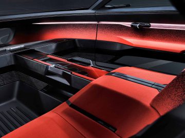 Futuristisch Audi Activesphere Concept-auto-interieur met rode stoelen, zwarte en rode lambrisering, een minimalistische middenconsole met bekerhouders en een strak, modern ontwerp.