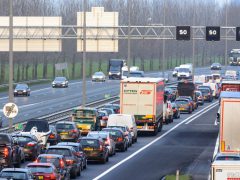 Zware verkeersopstoppingen op een snelweg met meerdere rijstroken, waar auto's en vrachtwagens overdag in de rij staan. Er strekt zich een dicht wagenpark uit, met op de achtergrond bomen en verschillende bovengrondse borden.