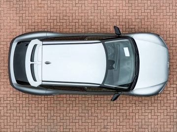 Een bovenaanzicht van een zilverkleurige personenauto met zwarte accenten, geparkeerd op een rode bakstenen stoep.