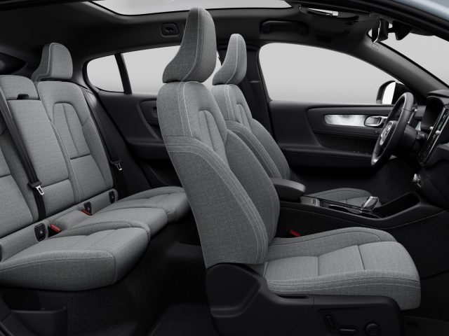 De afbeelding toont het interieur van een moderne Volvo-auto met achterwielaandrijving, voorzien van grijze stoffen stoelen, een strak dashboard en een middenconsole. De achterstoelen zijn voorzien van drie individuele hoofdsteunen en veiligheidsgordels.