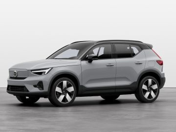 Op een inpandige betonvloer staat een grijze Volvo SUV met zwarte accenten en achterwielaandrijving geparkeerd. Het voertuig heeft een strak ontwerp met opvallende lichtmetalen velgen en een imperiaal. De achtergrond is effen en minimalistisch.