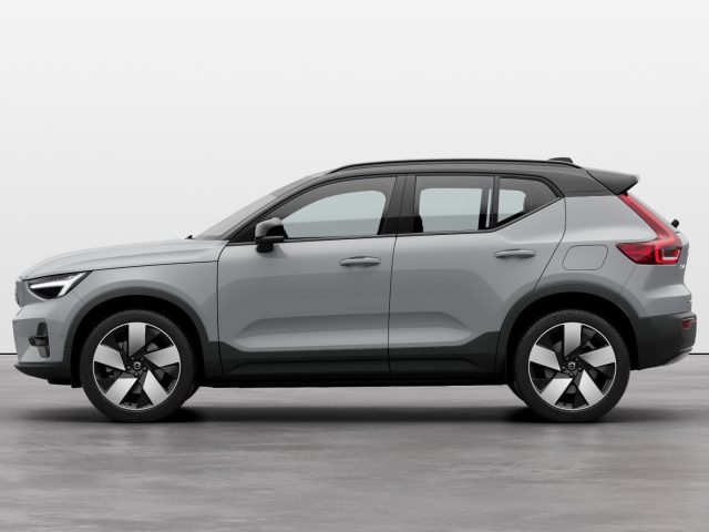 Zijaanzicht van een zilveren Volvo compacte SUV met zwarte bekleding, geparkeerd op een grijze ondergrond tegen een effen witte achtergrond. Dit model heeft een strak ontwerp en een betrouwbare achterwielaandrijving, perfect voor wie op zoek is naar stijl en prestaties.