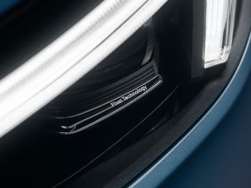 Close-up van de koplamp van een auto met de woorden 'Pixel Technology' erop gegraveerd, met gedetailleerde lichtelementen en een strak, modern ontwerp. Deze functie benadrukt Volvo's toewijding aan innovatie, perfect gecombineerd met hun vermaarde achterwielaandrijvingssysteem.