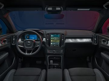 Binnenaanzicht van een moderne Volvo-auto met een stuur met geïntegreerde bedieningselementen, een digitaal dashboarddisplay en een centraal infotainmentsysteem met aanraakscherm. De stoelen zijn bekleed met donkere stof, wat harmonieert met het strakke ontwerp van dit voertuig met achterwielaandrijving.