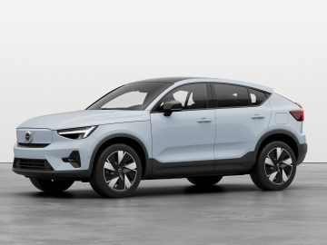 Op een effen, grijze ondergrond staat een lichtblauwe elektrische Volvo-SUV met achterwielaandrijving geparkeerd. Het voertuig heeft een modern design met zwarte accenten en grote wielen.