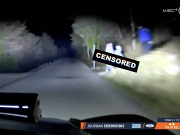 Een nachtelijke rallyrace vanuit het perspectief van de coureur, die doet denken aan een WRC-evenement, waarbij een 'gecensureerde' tag een deel van het beeld verduistert. Aan de rechterkant van de weg zijn enkele toeschouwers te zien.