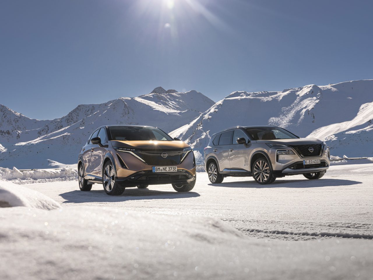 Twee voertuigen uitgerust met e-4ORCE-technologie staan geparkeerd in een besneeuwd landschap, tegen de achtergrond van met sneeuw bedekte bergen onder een helderblauwe lucht.