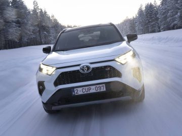 Een witte Toyota RAV4 SUV rijdt op een besneeuwde weg met bomen op de achtergrond.