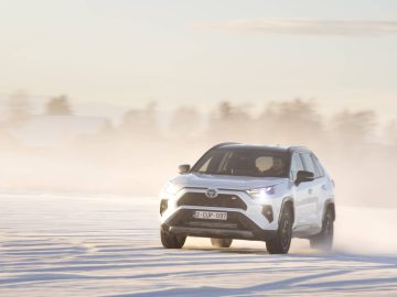 Een witte Toyota RAV4 SUV rijdt door een besneeuwd landschap met vage bomen op de achtergrond.