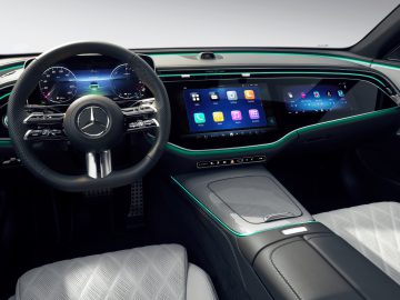 Het interieur van de Mercedes E-klasse 2023 straalt moderne luxe uit met een strak dashboard met meerdere digitale schermen, een gepolijst stuur met bedieningselementen en verlichte accenten. De stoelen zijn bekleed met wit leer voor een extra vleugje elegantie.