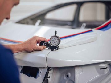 Een persoon gebruikt een meetklok om de pasvorm en uitlijning op de motorkap van een witte BMW 3.0 CSL te meten.