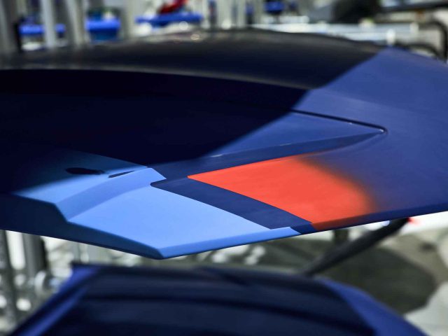 Close-up van een abstracte sculpturale installatie met gelaagde blauwe en rode geometrische vormen, die doen denken aan de dynamische lijnen van een BMW 3.0 CSL, met vage metalen structuren op de achtergrond.