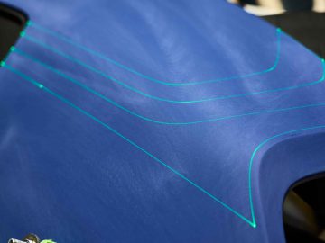 Close-up van een blauw oppervlak met drie parallelle neongroene lijnen erop, die doen denken aan de strakke designdetails die vaak te zien zijn in BMW 3.0 CSL-modellen, waarschijnlijk onderdeel van een technisch of ontwerpproces.