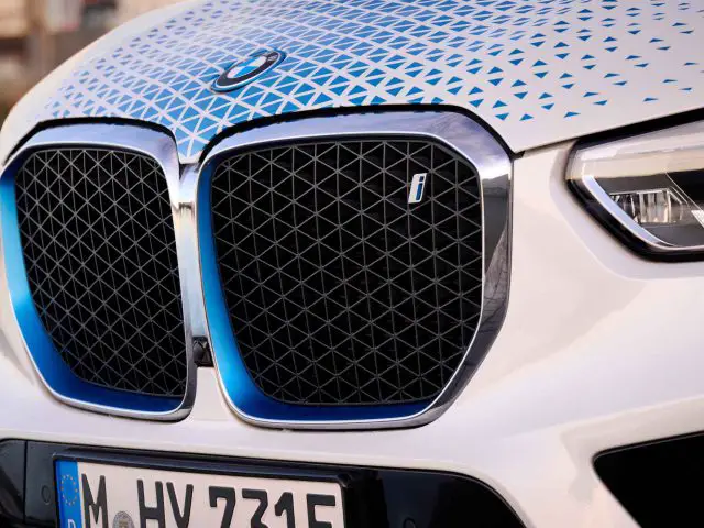 Close-up van de grille en koplamp van een BMW iX5 Hydrogen, met een geometrisch patroonontwerp en een Europees kenteken met de tekst "M HY 7315".