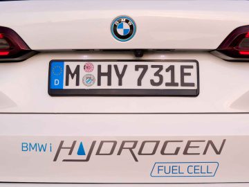 Close-up van de achterkant van een BMW iX5 Hydrogen-auto met een kentekenplaat met de tekst "MO HY 731E", met een "BMW i Hydrogen Fuel Cell"-logo en tekst.