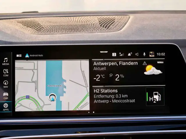 Het dashboarddisplay van een BMW iX5 Hydrogen toont een navigatiekaart met routebeschrijving naar Antwerpen, weersinformatie, temperatuur van -2°C en 2% kans op neerslag. In een sectie worden H2-stations belicht, waarvan er één gunstig gelegen is op 0,3 km afstand.