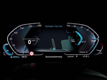 Het digitale autodashboard van de BMW iX5 Hydrogen geeft de status van een waterstofbrandstofcel weer, een snelheidsmeter bij 0 km/u en een bereik van 500 km. Het scherm toont ook de tijd, temperatuur en verschillende voertuigindicatoren in blauwe accenten.