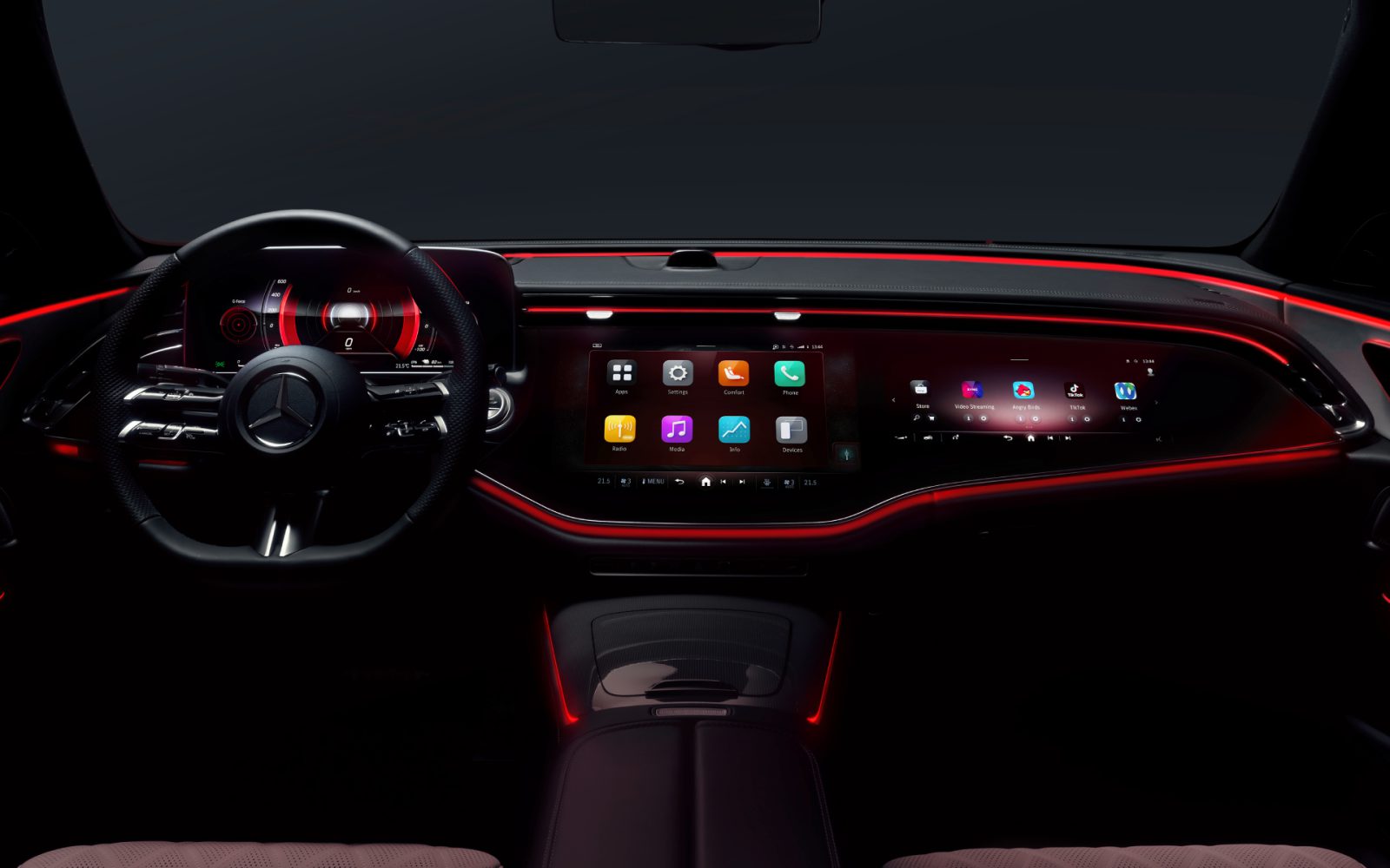 Dashboard van een Mercedes E-klasse 2023 's nachts met een strak digitaal display met verschillende applicaties, een futuristisch stuur en rode sfeerverlichting.