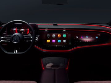 Dashboard van een Mercedes E-klasse 2023 's nachts met een strak digitaal display met verschillende applicaties, een futuristisch stuur en rode sfeerverlichting.