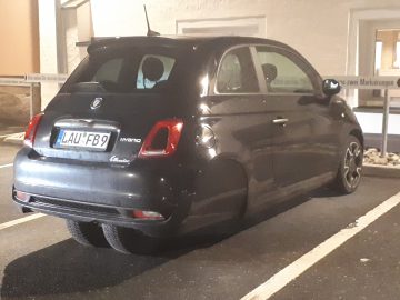 Een zwarte Fiat 500 Hybrid Ellenator staat geparkeerd op een aangewezen parkeerplaats op een buitenterrein. Het voertuig, met kenteken "LAU-FB9", valt op tussen de omringende voertuigen.