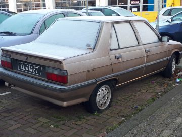 Een met vorst bedekte bruine Renault 9 sedan staat op een ijskoude ochtend naast andere voertuigen geparkeerd op een parkeerplaats.