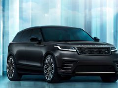 Een zwarte Range Rover Velar SUV geparkeerd voor een futuristische, lichtblauwe achtergrond met reflecterende oppervlakken.