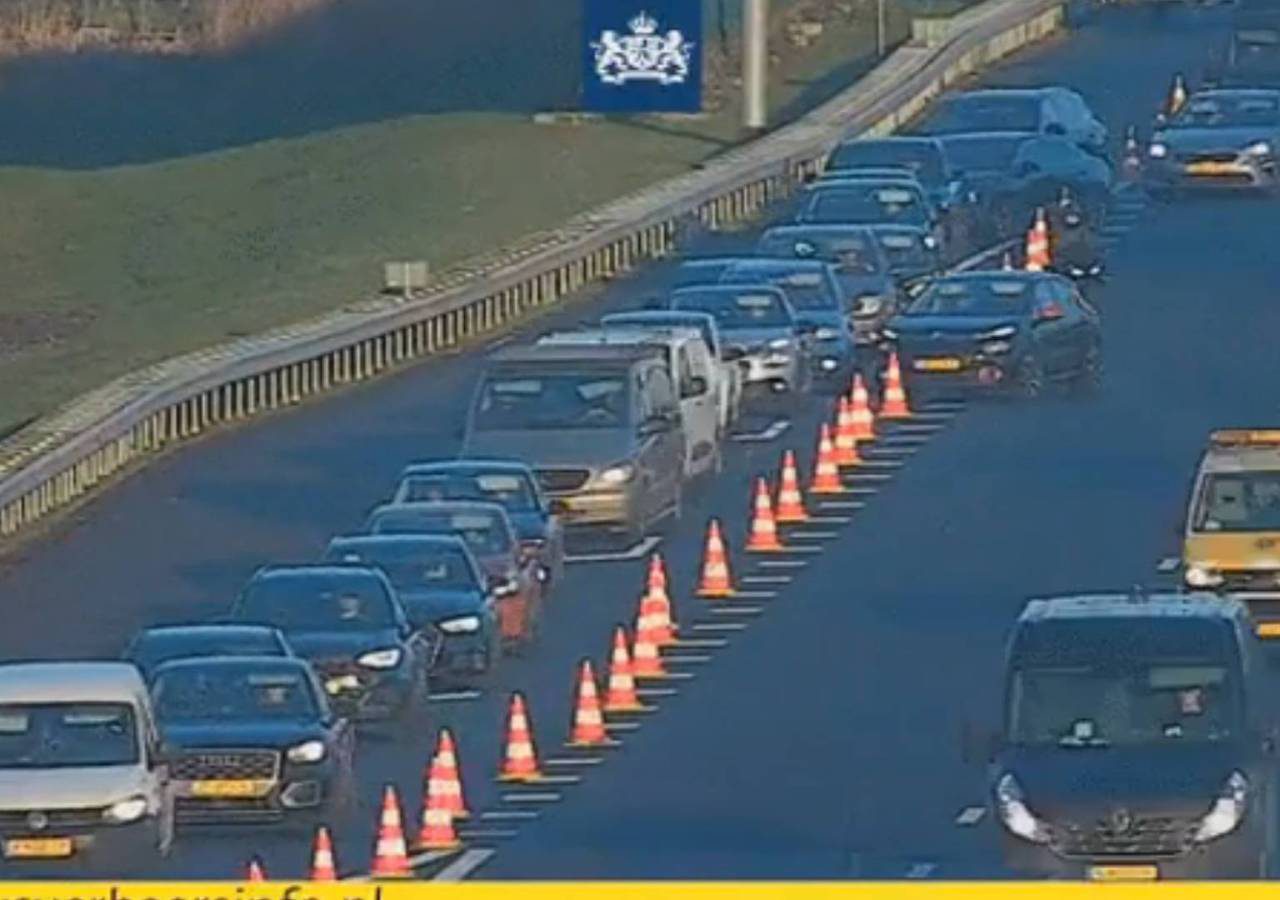 Het verkeer rijdt langzaam op de A20, een snelweg met meerdere rijstroken, met veel auto's in de rij achter oranje verkeerskegels. Aan de rechterkant van de afbeelding is een wegonderhoudsvoertuig te zien.