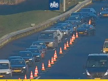 Het verkeer rijdt langzaam op de A20, een snelweg met meerdere rijstroken, met veel auto's in de rij achter oranje verkeerskegels. Aan de rechterkant van de afbeelding is een wegonderhoudsvoertuig te zien.