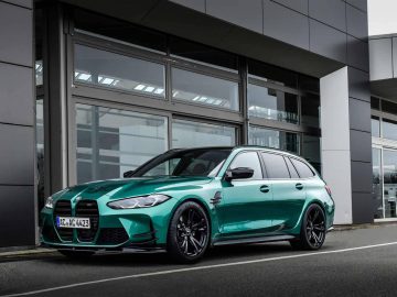 Een groene M3 Touring staat geparkeerd voor een modern gebouw met grote ramen, wat het strakke ontwerp en de sportieve kenmerken benadrukt.