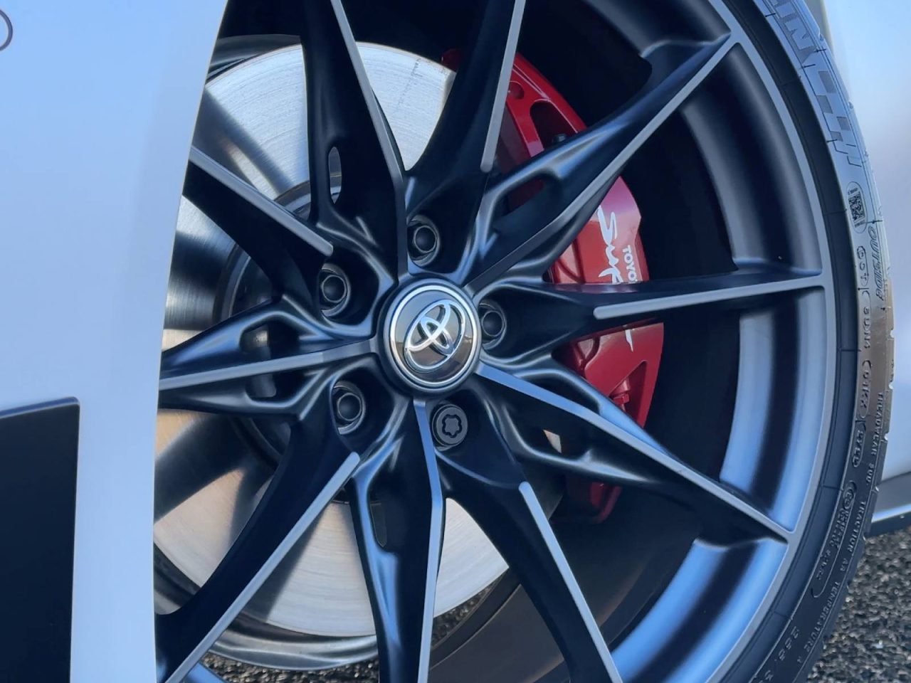 Close-up van een zwart Velgen-lichtmetalen autowiel met een zichtbare rode remklauw en band, gemonteerd op een voertuig.