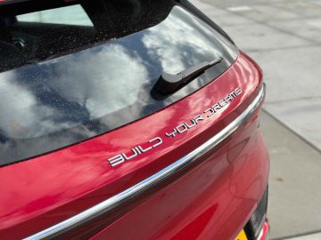 Close-up van de achterkant van een rode BYD Atto 3 met de tekst "BUILD YOUR DREAMS" op de achterkant. De auto staat geparkeerd op een verhard oppervlak, waardoor het strakke ontwerp is vastgelegd voor onze gedetailleerde beoordeling.
