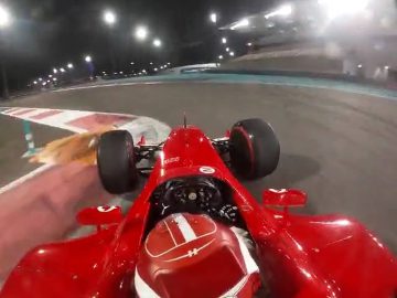 Een rode raceauto met een krachtige V10-motor snelt 's nachts de bocht om op een racecircuit, terwijl de lichten de baan verlichten. Uitzicht van boven de bestuurdersstoel.