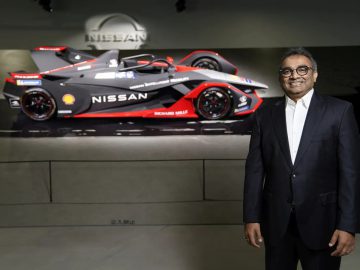 Een man in pak staat naast een Formule E-raceauto van Nissan, die zwart, rood en zilver is en versierd met opvallende emblemen.