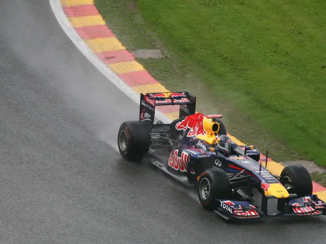 Een Red Bull Formule 1-auto, bestuurd door de Nederlandse Max Verstappen, snelt tijdens een race op een nat circuit met rode, gele en witte stoepranden.