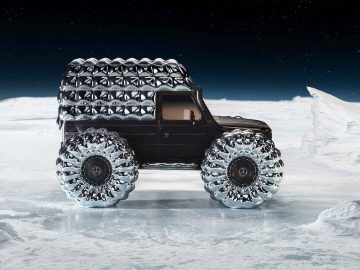 Een donkere SUV, onderdeel van Project Mondo G, met grote, futuristische, transparante banden en een metalen, gewatteerd dak staat geparkeerd in een besneeuwd, ijzig landschap onder een heldere nachtelijke hemel.