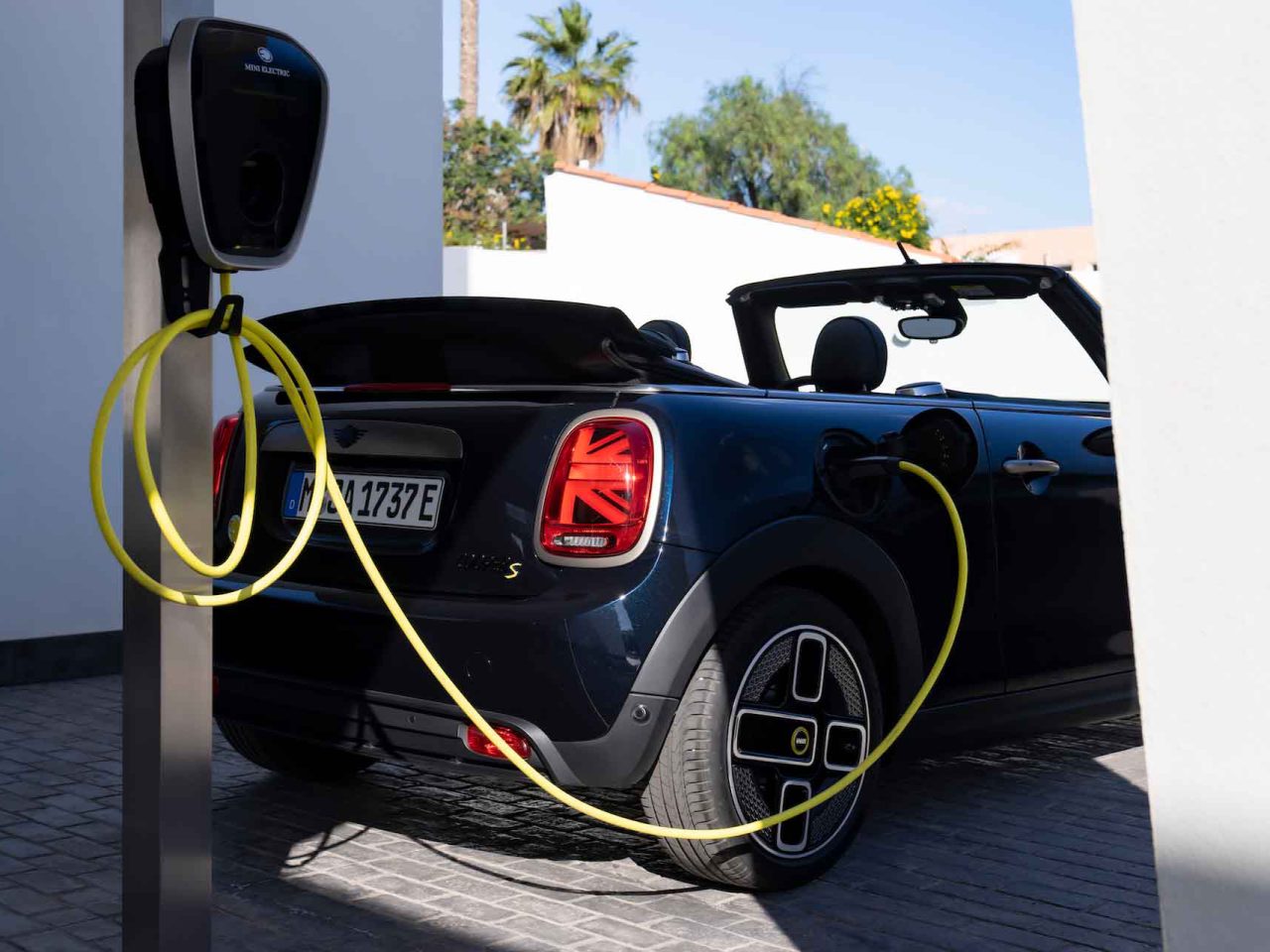 Een zwarte MINI Electric Cabrio met gele laadkabel is buiten aangesloten op een wandlader.