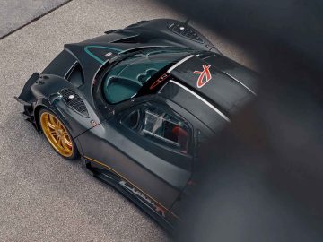 Bovenaanzicht van een hoogwaardige zwarte Pagani Zonda R Evo met gouden wielen, een carrosserie van koolstofvezel en een aerodynamisch ontwerp. De auto staat geparkeerd op een betonnen ondergrond.