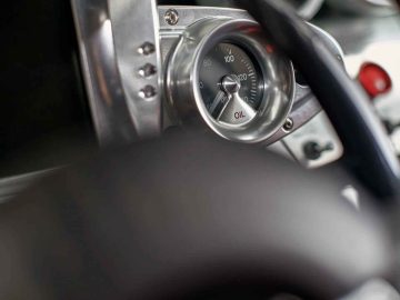 Close-up van een oliedrukmeter in een Pagani Zonda R Evo-dashboard, met een bereik van 0 tot 100. De voorgrond is wazig, waardoor de aandacht wordt gevestigd op de meter en het omringende metalen paneel.