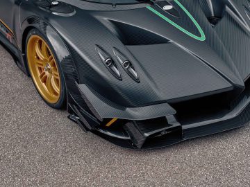 Close-up van de voorkant van een Pagani Zonda R Evo in zwart koolstofvezel met gouden wielen, met hoekige designelementen, aerodynamische vinnen en groene accentlijnen op de motorkap.