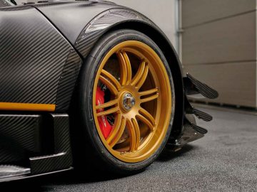 Close-up van het gouden lichtmetalen velg van een Pagani Zonda R Evo met een zichtbare rode remklauw en spatborddetails van koolstofvezel.