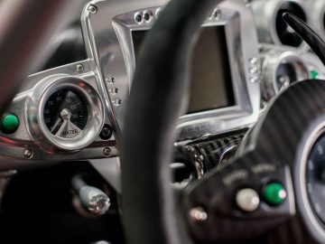 Close-up van het dashboard van een Pagani Zonda R Evo met een snelheidsmeter, een digitaal beeldscherm en verschillende bedieningsknoppen en schakelaars.