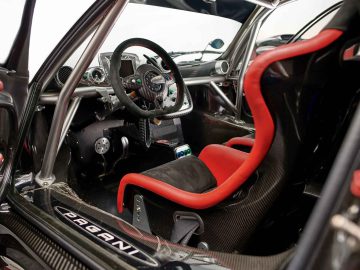 Binnenaanzicht van een Pagani Zonda R Evo-sportwagen, met het stuur, de rood-zwarte racestoel, de pedalen en de bedieningselementen op het dashboard.