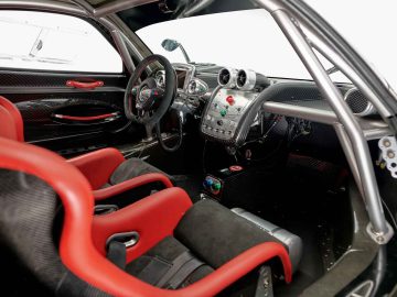 Het interieur van de Pagani Zonda R Evo-sportwagen is voorzien van opvallende rode en zwarte kuipstoelen, een stuur met meerdere bedieningselementen en een dashboard versierd met verschillende meters en schakelaars.