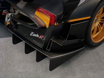 Close-up van het onderste achtergedeelte van een Pagani Zonda R Evo, met koolstofvezeldetails, diffuser aan de achterkant, amberkleurig achterlicht en goudkleurige wielen.