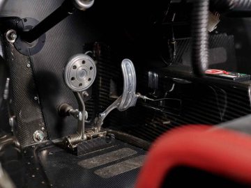 Close-up van de voetenruimte aan de bestuurderszijde van een auto met zichtbare metalen gas-, rem- en koppelingspedalen, gelegen in het donkere koolstofvezelinterieur van een Pagani Zonda R Evo.