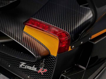 Close-up van de achterkant van een zwarte Pagani Zonda R Evo-supercar, met de nadruk op de koolstofvezeldetails, het rode en gele achterlicht en de aerodynamische kenmerken.