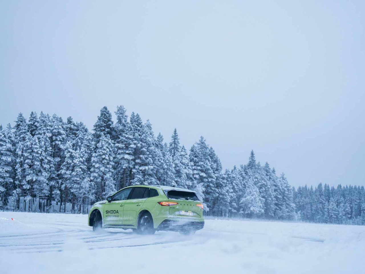 Een groene auto met het merk Skoda rijdt door een besneeuwd landschap, met op de achtergrond besneeuwde bomen.