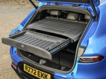 Een blauwe Tonale met open kofferbak onthult een uitschuifbare schuifplank en een zwarte kentekenplaat met de tekst "RZ72 EKK.