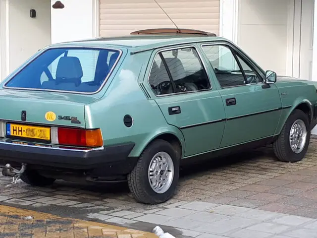 Een groene vierdeurs hatchback van DAF staat geparkeerd op een oprit naast een huisgarage met een blauw 'service'-bord aan de muur.