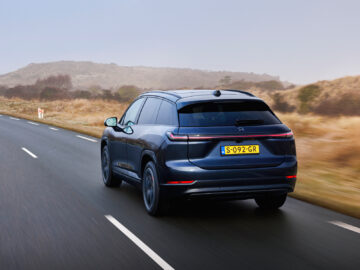 Een donkergekleurde NIO EL7 SUV met kenteken S-092-GR rijdt op een landweg met met gras begroeide heuvels op de achtergrond.